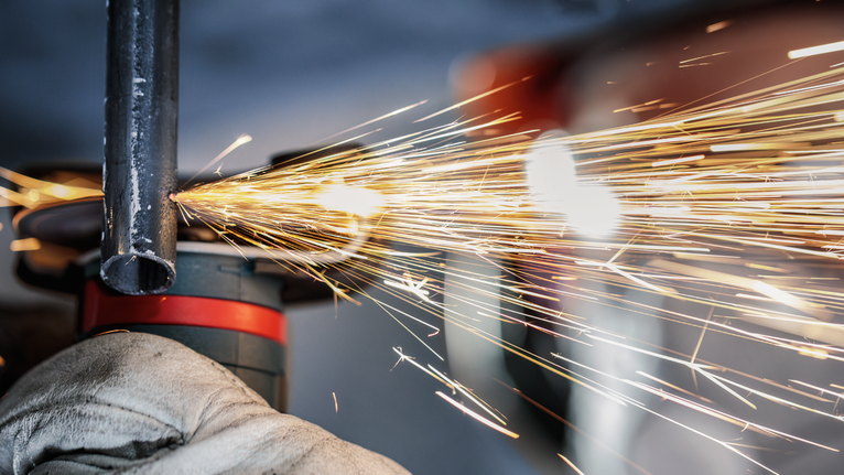 บุคคลที่สวมอุปกรณ์ความปลอดภัยกำลังบดท่อโลหะ ทำให้เกิดประกายไฟสว่าง