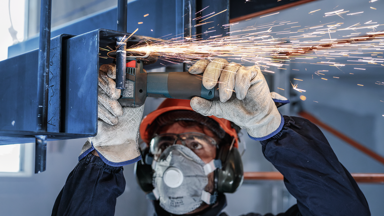 บุคคลที่สวมอุปกรณ์ความปลอดภัยทำการบดโลหะ ทำให้เกิดประกายไฟ