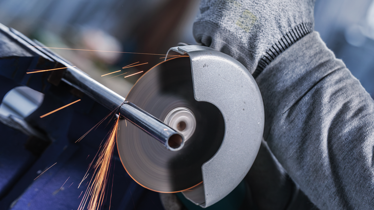 บุคคลที่สวมอุปกรณ์ความปลอดภัยกำลังตัดท่อโลหะด้วยเครื่องมือเจียร