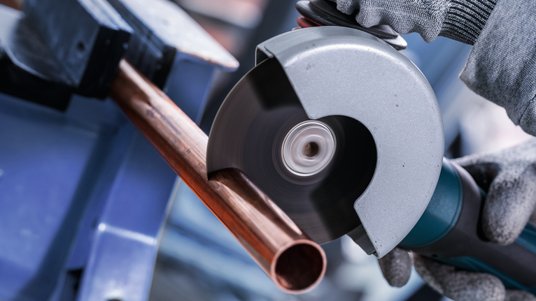 บุคคลที่สวมอุปกรณ์ความปลอดภัยตัดท่อทองแดงด้วยเครื่องเจียรแบบมุม