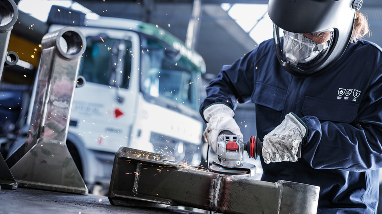 บุคคลที่สวมอุปกรณ์ความปลอดภัยทำการบดโลหะ ทำให้เกิดประกายไฟ