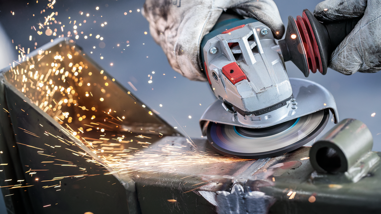 บุคคลที่สวมอุปกรณ์ความปลอดภัยทำการเจียรโลหะ ทำให้เกิดประกายไฟสว่าง