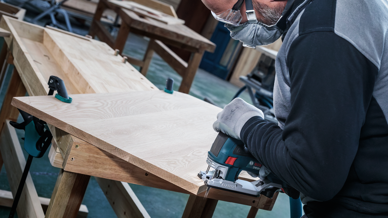 บุคคลที่สวมอุปกรณ์ความปลอดภัยใช้จิ๊กซอว์ตัดแผ่นไม้