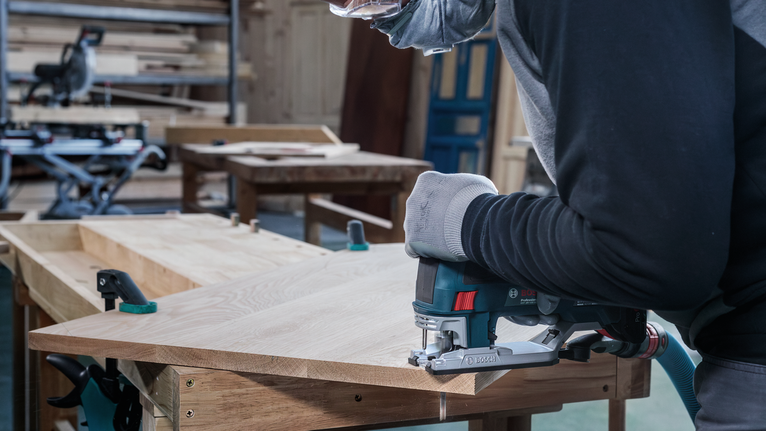 คนสวมอุปกรณ์ป้องกันความปลอดภัยกำลังตัดไม้ด้วยจิ๊กซอว์ในโรงงาน