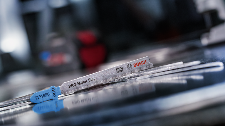 ใบเลื่อยจิ๊กซอว์โลหะวางอยู่บนพื้นผิวโลหะสะท้อนแสงในโรงงาน