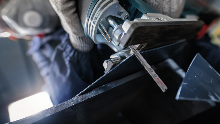 บุคคลที่สวมอุปกรณ์ความปลอดภัยกำลังตัดโลหะด้วยจิ๊กซอว์