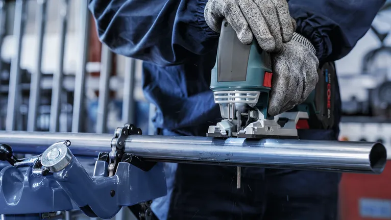 บุคคลที่สวมอุปกรณ์ความปลอดภัยใช้จิ๊กซอว์ตัดท่อเหล็ก