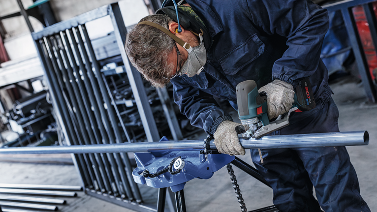 บุคคลที่สวมอุปกรณ์ความปลอดภัยกำลังเจียรท่อโลหะในโรงงานอุตสาหกรรม