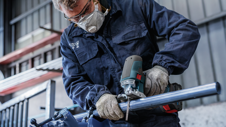 บุคคลที่สวมอุปกรณ์ความปลอดภัยกำลังตัดท่อโลหะด้วยจิ๊กซอว์