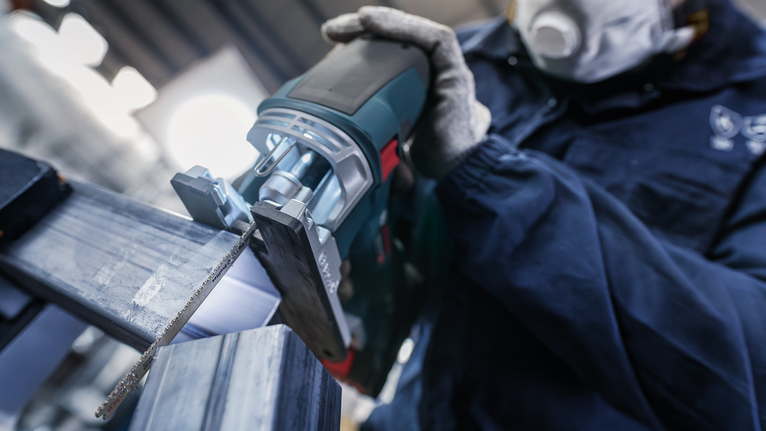 บุคคลที่สวมอุปกรณ์ด้านความปลอดภัยใช้เลื่อยตัดโลหะแบบลูกสูบ