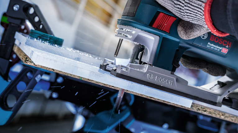 บุคคลที่สวมอุปกรณ์ความปลอดภัยกำลังตัดแผ่นพลาสติกด้วยจิ๊กซอว์