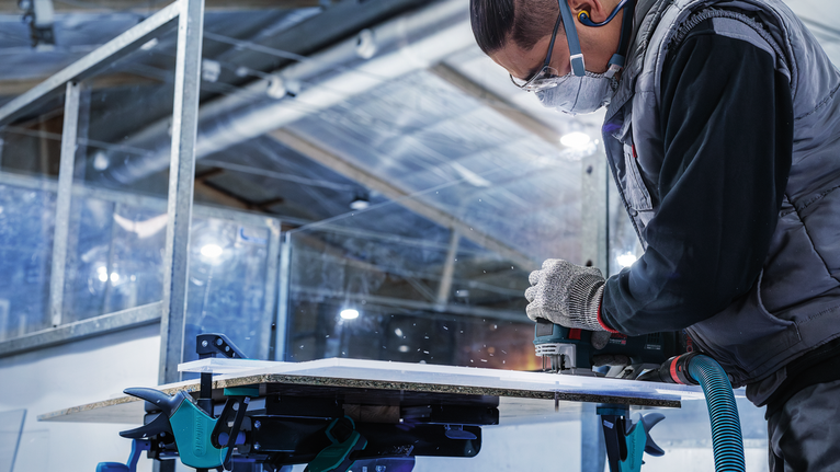 บุคคลที่สวมอุปกรณ์ความปลอดภัยใช้เครื่องมือไฟฟ้าตัดแผ่นไม้