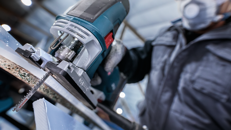 บุคคลที่สวมอุปกรณ์ความปลอดภัยใช้จิ๊กซอว์ตัดชิ้นวัสดุ