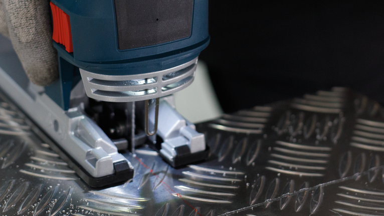 ผู้ที่สวมอุปกรณ์ความปลอดภัยกำลังใช้งานจิ๊กซอว์เพื่อตัดแผ่นโลหะที่มีลวดลาย