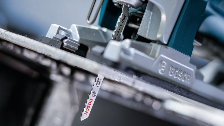 ภาพระยะใกล้ของใบเลื่อยจิ๊กซอว์ที่กำลังตัดผ่านแผ่นโลหะ