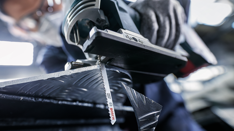 บุคคลที่สวมอุปกรณ์ความปลอดภัยกำลังตัดโลหะที่มีลวดลายด้วยจิ๊กซอว์