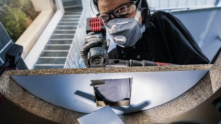 บุคคลที่สวมอุปกรณ์ความปลอดภัยกำลังเจาะรูบนแผ่นไม้