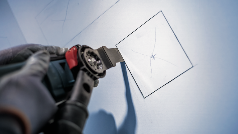 บุคคลที่สวมอุปกรณ์ด้านความปลอดภัยใช้เครื่องมือไฟฟ้าตัดแผ่นยิปซัมให้เป็นสี่เหลี่ยมจัตุรัส