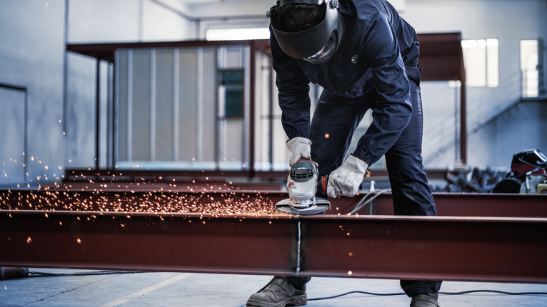 บุคคลที่สวมอุปกรณ์ความปลอดภัยบดคานโลหะทำให้เกิดประกายไฟ