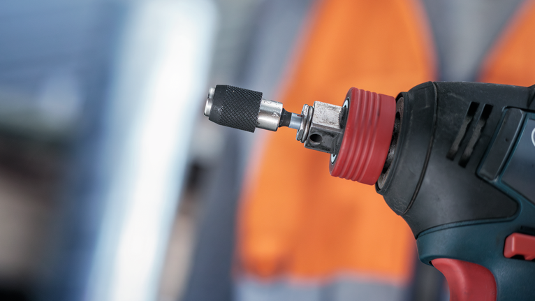 ภาพแสดงเครื่องมือไฟฟ้าพร้อมดอกสว่านโลหะ โดยมีบุคคลอยู่เบื้องหลังสวมอุปกรณ์ป้องกันความปลอดภัย