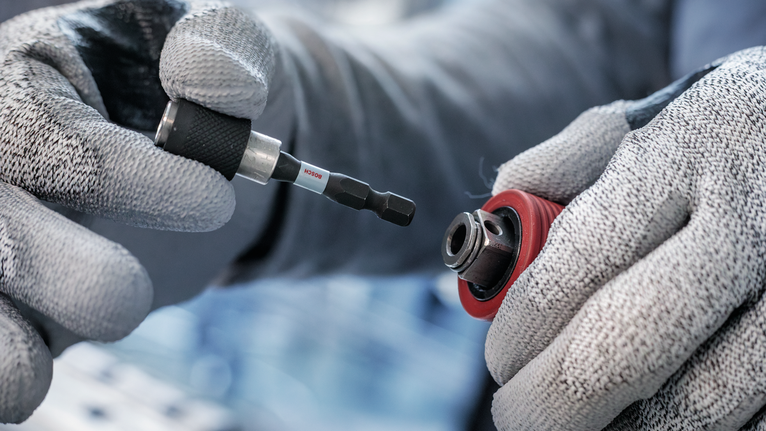 บุคคลที่สวมอุปกรณ์ด้านความปลอดภัยกำลังเสียบดอกไขควงเข้าไปในหัวจับดอกสว่าน