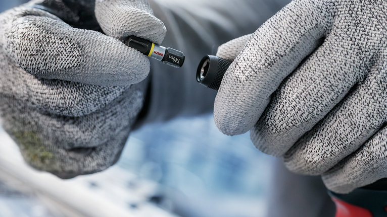 บุคคลที่สวมอุปกรณ์ด้านความปลอดภัยถือดอกไขควงไว้ใกล้กับหัวสว่าน