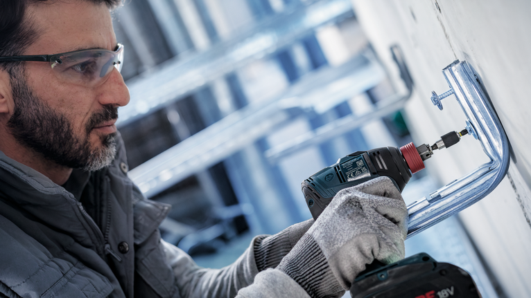 บุคคลที่สวมอุปกรณ์ด้านความปลอดภัยติดตั้งตัวยึดโลหะโดยใช้สว่านไร้สาย