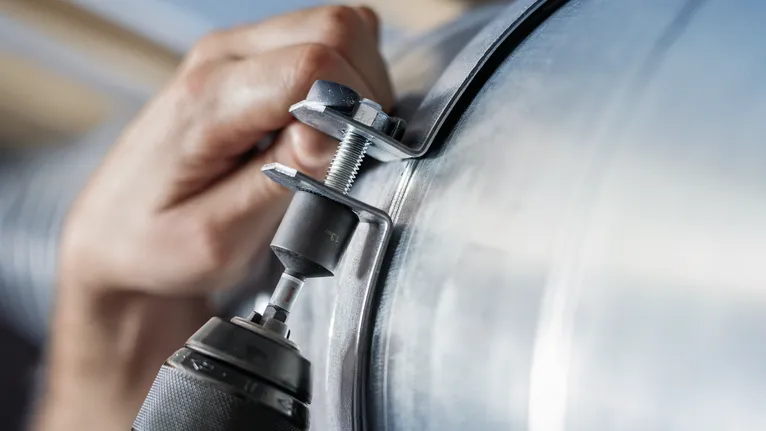 บุคคลกำลังยึดที่หนีบโลหะเข้ากับท่อโดยใช้เครื่องมือไฟฟ้า