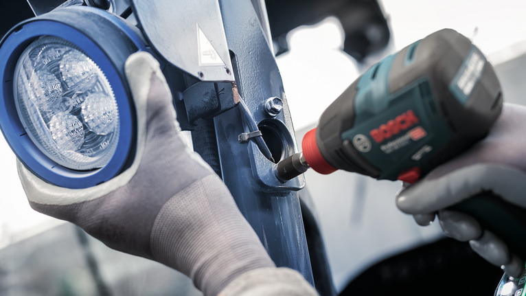 บุคคลที่สวมอุปกรณ์ด้านความปลอดภัยใช้เครื่องมือไฟฟ้าเพื่อยึดตัวยึดโลหะใกล้กับไฟ