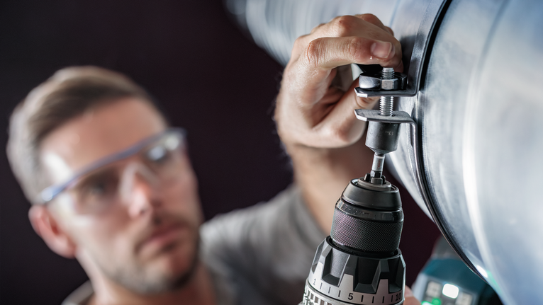 บุคคลที่สวมอุปกรณ์ความปลอดภัยกำลังเจาะรูในท่อโลหะขนาดใหญ่