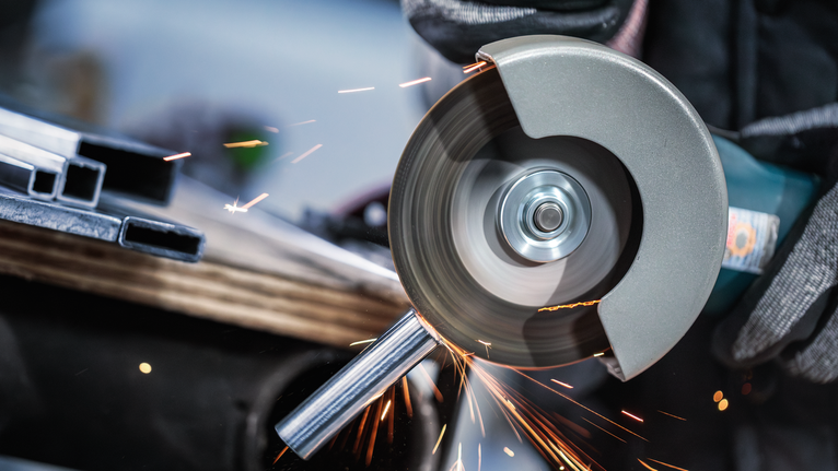 บุคคลที่สวมอุปกรณ์ความปลอดภัยใช้เครื่องเจียรตัดท่อโลหะ