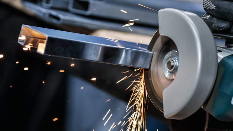 บุคคลที่สวมอุปกรณ์ความปลอดภัยทำการเจียรโลหะ ทำให้เกิดประกายไฟสว่าง