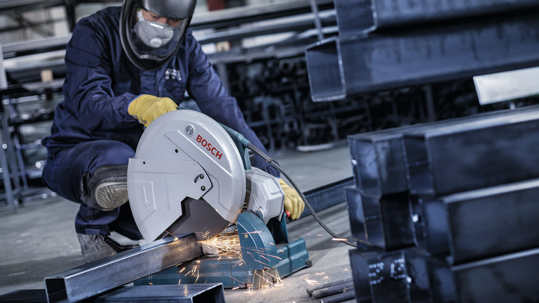 คนงานที่สวมอุปกรณ์ความปลอดภัยกำลังตัดท่อโลหะด้วยเลื่อยไฟฟ้า ทำให้เกิดประกายไฟ.