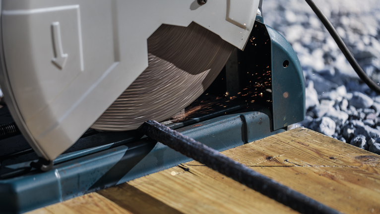 เลื่อยตัดไม้กำลังตัดผ่านแท่งโลหะบนแท่นไม้