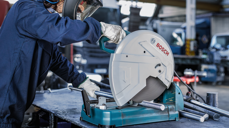 บุคคลที่สวมอุปกรณ์ความปลอดภัยกำลังใช้เลื่อยวงเดือนตัดท่อโลหะ