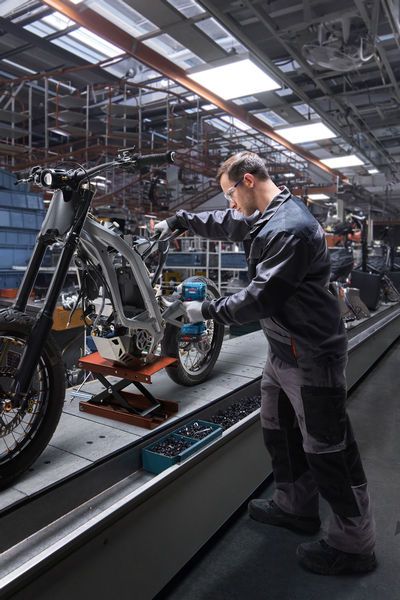 ผู้ที่สวมอุปกรณ์ด้านความปลอดภัยใช้ไขควงกระแทกในการประกอบโครงรถจักรยานยนต์.