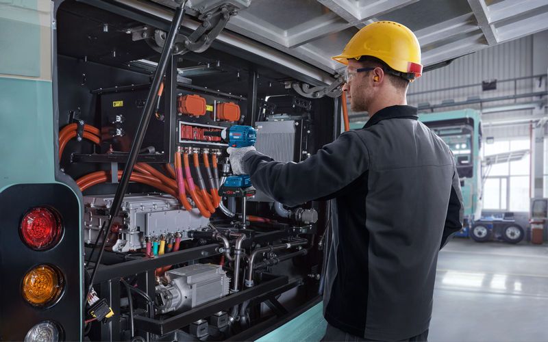 บุคคลที่สวมอุปกรณ์ด้านความปลอดภัยใช้ประแจกระแทกกับเครื่องยนต์รถโดยสารไฟฟ้า.