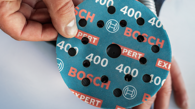 บุคคลกำลังวางแผ่นขัดแบบกลมไว้บนเครื่องมือ.