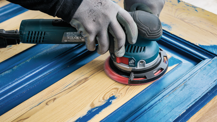 ผู้ที่สวมอุปกรณ์ความปลอดภัยกำลังขัดสีฟ้าออกจากประตูไม้