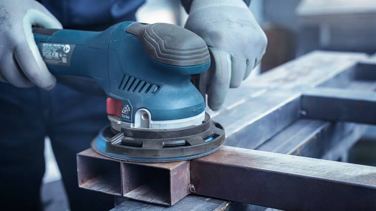 บุคคลที่สวมอุปกรณ์ป้องกันความปลอดภัยกำลังขัดพื้นผิวโลหะด้วยเครื่องขัดไฟฟ้า