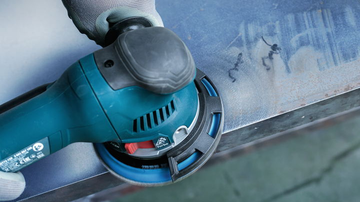 บุคคลที่สวมอุปกรณ์ด้านความปลอดภัยกำลังขัดพื้นผิวโลหะด้วยเครื่องมือไฟฟ้า