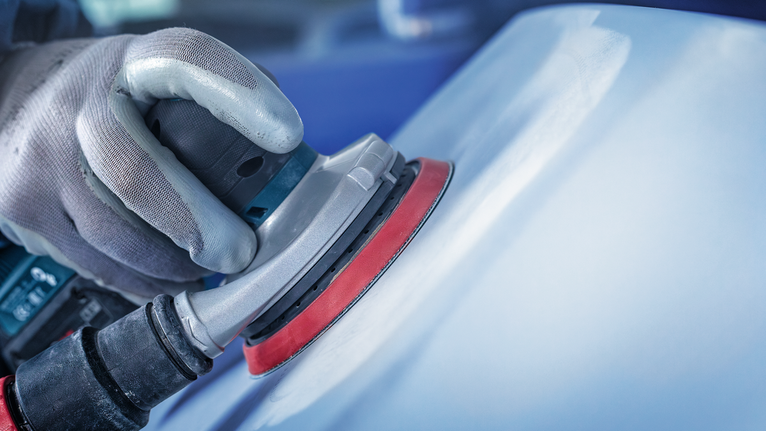 บุคคลที่สวมอุปกรณ์ความปลอดภัยกำลังขัดพื้นผิวรถยนต์ด้วยเครื่องขัดไฟฟ้า