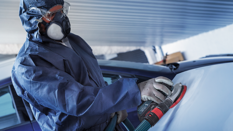บุคคลที่สวมอุปกรณ์ด้านความปลอดภัยกำลังขัดพื้นผิวรถยนต์ด้วยเครื่องขัดไฟฟ้า