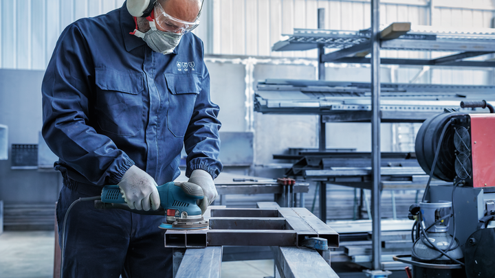 บุคคลที่สวมอุปกรณ์ความปลอดภัยกำลังบดคานโลหะในโรงงานอุตสาหกรรม