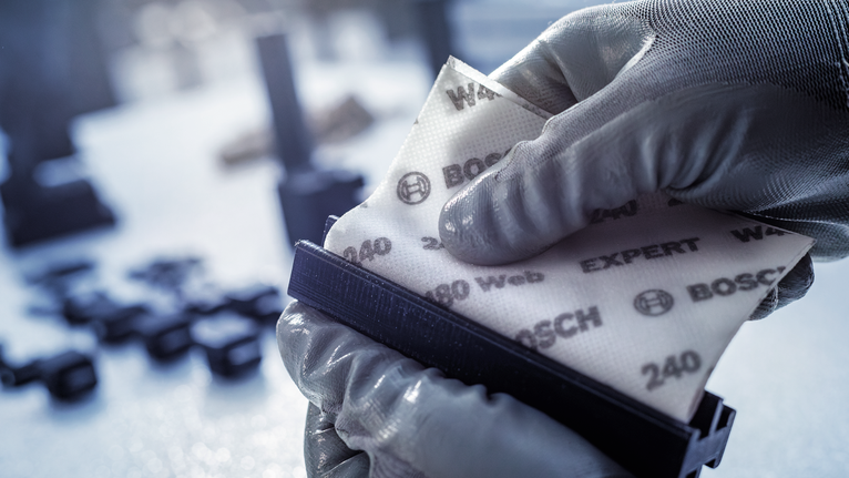 บุคคลที่สวมอุปกรณ์ด้านความปลอดภัยกำลังติดกระดาษทรายชนิดหยาบเข้ากับบล็อกขัด