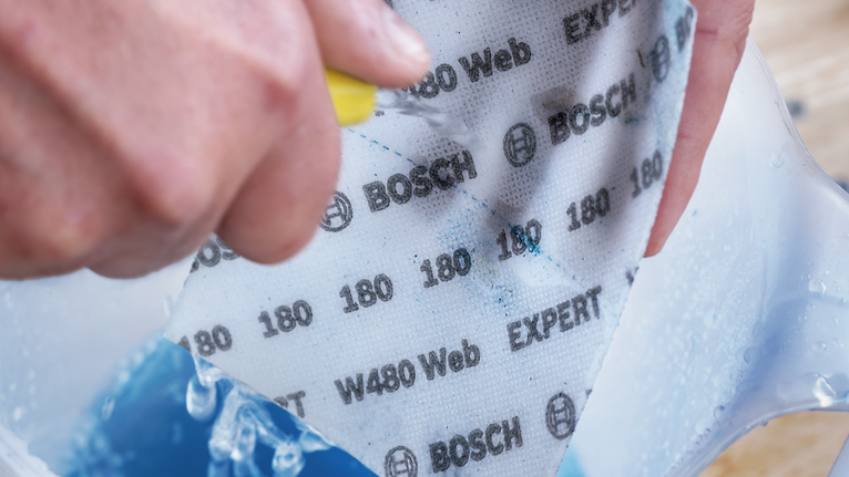 บุคคลที่สวมอุปกรณ์ป้องกันความปลอดภัยกำลังทำให้กระดาษทรายที่มีฤทธิ์กัดกร่อนเปียกและขัดถูในภาชนะ