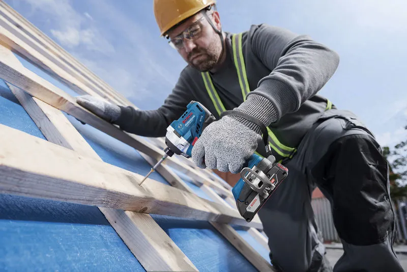 บุคคลที่สวมอุปกรณ์ด้านความปลอดภัยใช้สว่านไร้สายในการขันสกรูเข้าไปในคานไม้.