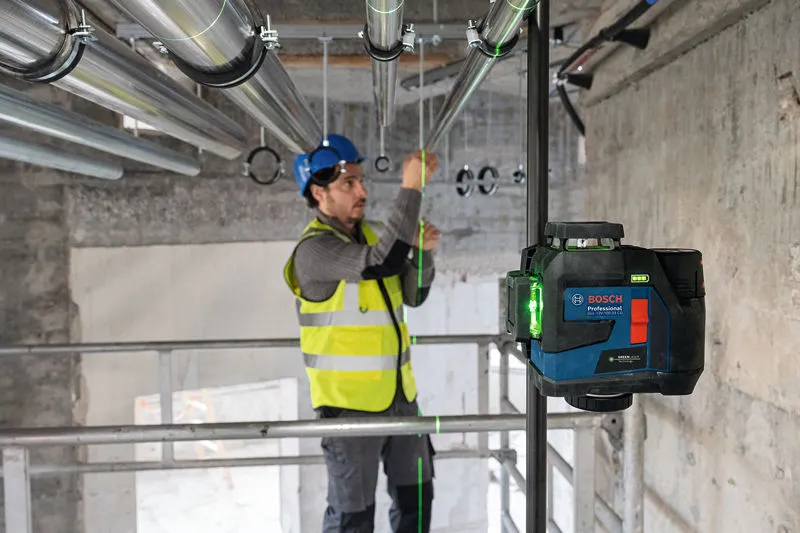 บุคคลที่สวมอุปกรณ์ด้านความปลอดภัยกำลังจัดแนวท่อโดยใช้เครื่องมือปรับระดับด้วยเลเซอร์.