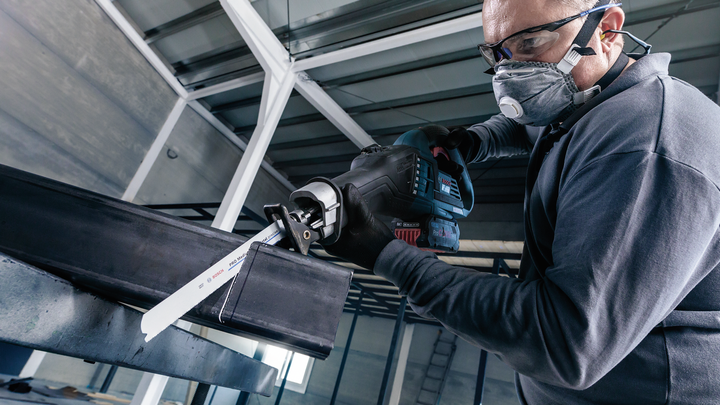 บุคคลที่สวมอุปกรณ์ด้านความปลอดภัยใช้เลื่อยตัดโลหะแบบลูกสูบ