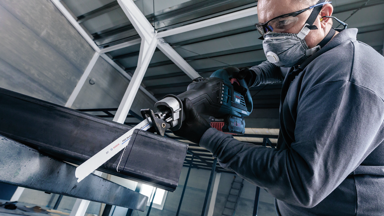 บุคคลที่สวมอุปกรณ์ด้านความปลอดภัยใช้เลื่อยตัดโลหะแบบลูกสูบ